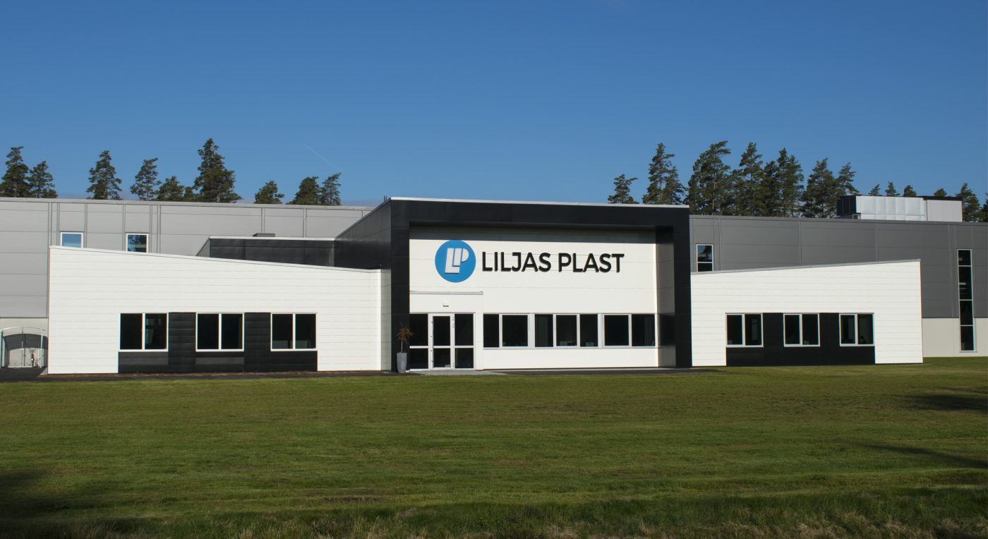 Modern fastighet med LED-skylt för Liljas Plast i Hillerstorp, omgiven av grön gräsmatta och en blå himmel