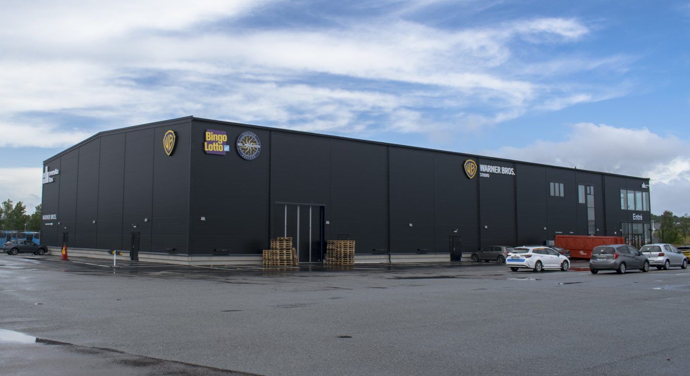 Stor grå fastighet i Göteborg med fasadskyltar och ljuslådor för Warner Bros, Bingolotto, Postkodmiljonären och Svenska Hus. Blå himmel med vita moln i bakgrunden