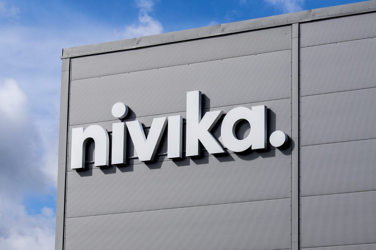 Nivikas vita genomlysande fasadskylt monterad på en grå fasad med en blå himmel i bakgrunden
