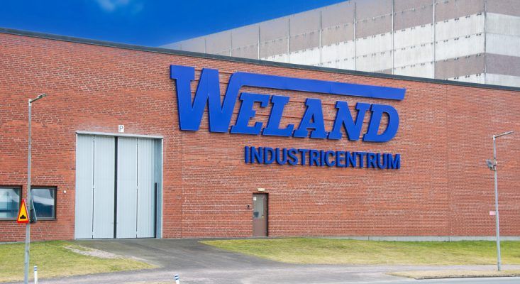 Stora blå bokstäver med texten Weland Industricentrum på en röd tegelfasad.